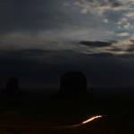 Moon rises over Monument Valley as vehicle moves slowly on dirt road passing buttes